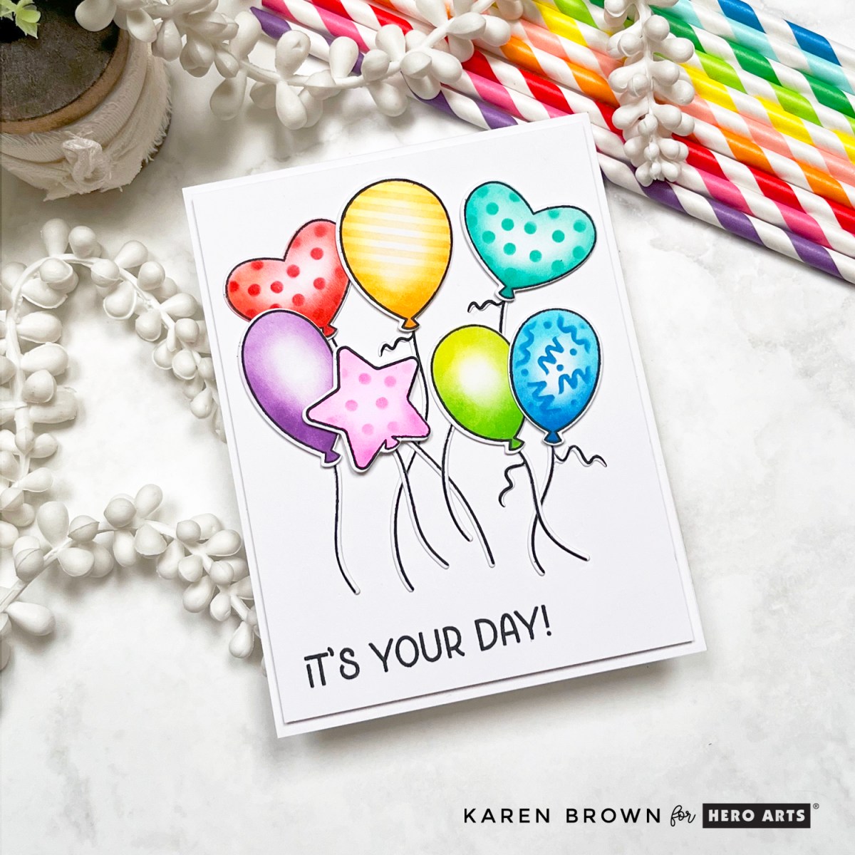 A handmade card with seven colorful stenciled balloons in rainbow colors, layered with foam tape. Balloons feature squiggles, dots, and stripes. Sentiment reads "It’s Your Day!"

