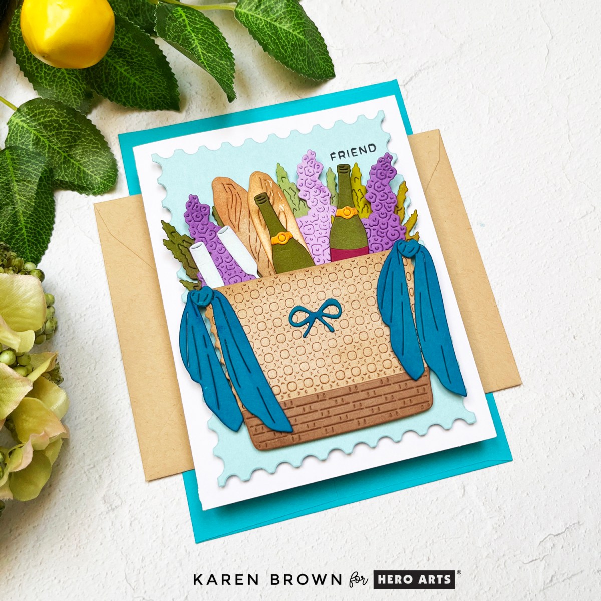 Hero Arts June 2025 Card Kit of the Month card featuring a tan picnic basket filled with baguette bread, wisteria flowers, wine glasses and two bottles of wine.