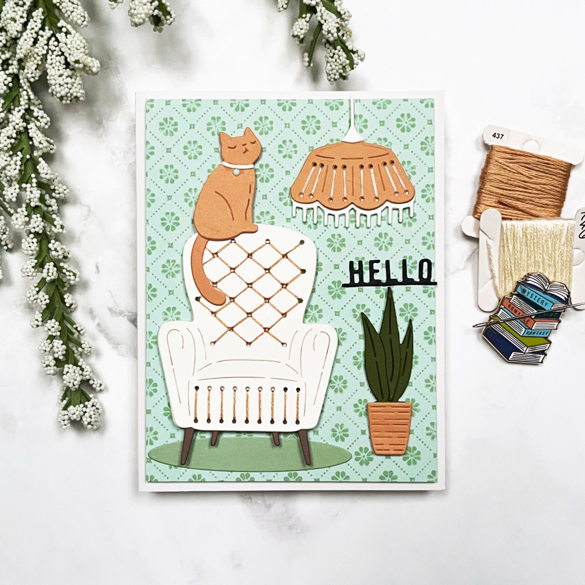 Cozy Scene Card: Handmade card showing a stitched cream armchair with a stitched hanging light, orange tabby cat, and potted plant. Background stamped with mint wallpaper pattern.