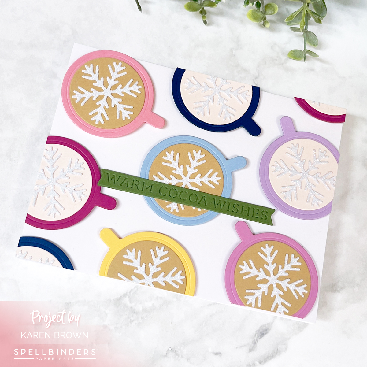 An assortment of brightly colored cocoa mugs with glittery snowflake toppers, some mugs trimmed at the edge for a dynamic layout. The sentiment reads 'Warm Cocoa Wishes