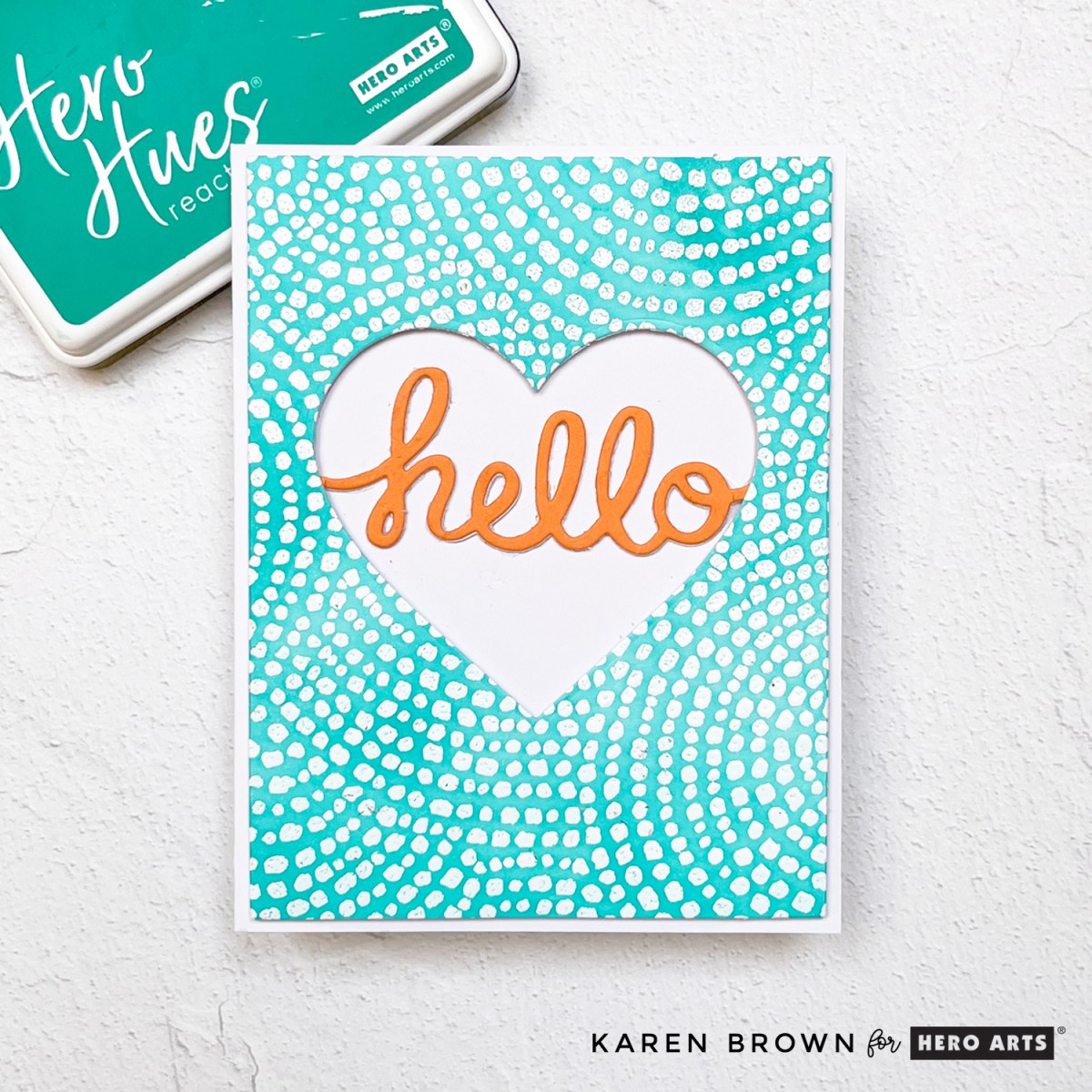 Aqua blue and white heat embossed and ink-blended Cobblestone Courtyard background card with die cut heart window and a scripty orange “hello” sentiment..
