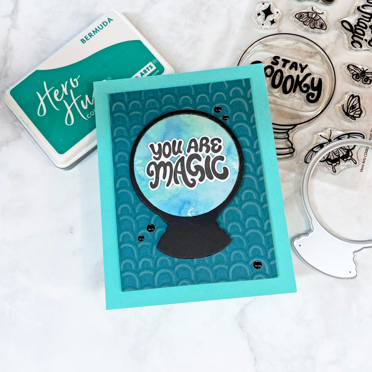 Card featuring a die cut crystal ball made from ink smooshed background and acetate layer, with the sentiment “You Are Magic” over a tone-on-tone mini rainbow background stenciled in teal and aqua shades.