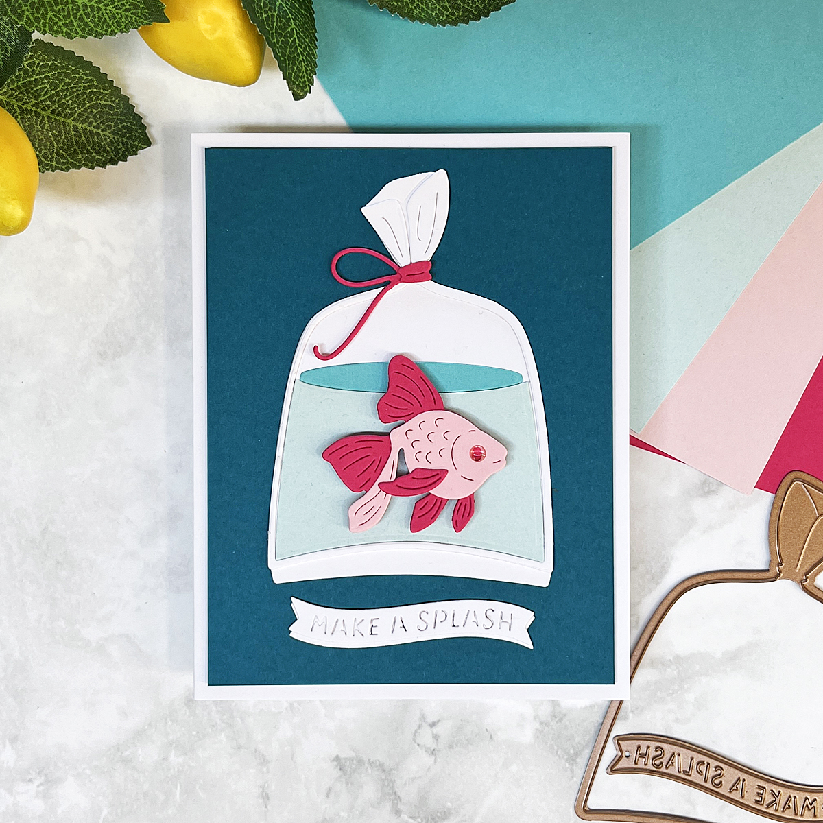 Pink fish in a plastic bag on blue background with “Make a Splash” sentiment. Made with Spellbinders August 2025 Large Die of the Month.