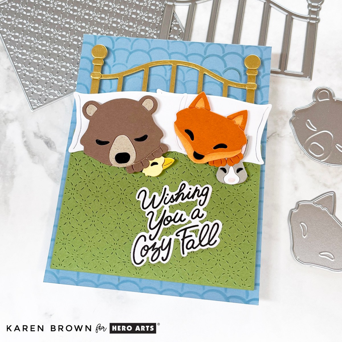 Adorable die cut scene card featuring an adorable brown bear and red fox snuggling in a brass bed with their stuffed animals.  Created with the Hero Arts September 2025 Fancy Die Kit of the Month:  Cozy Critters.  