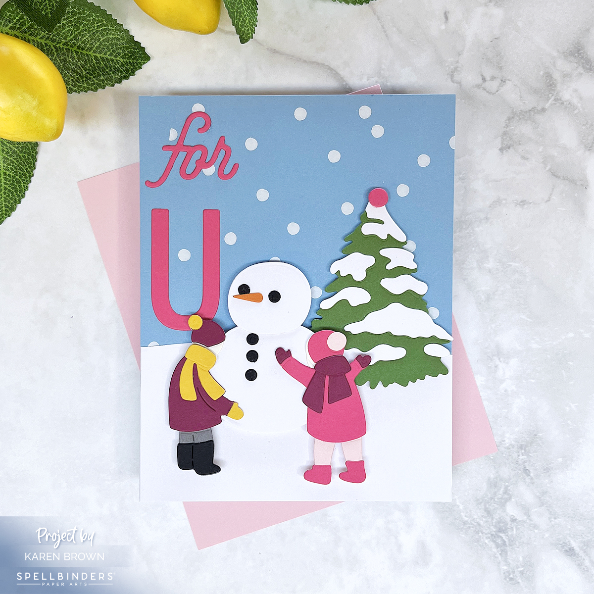 Handmade winter card featuring a girl in pink and a boy in burgundy and yellow building a snowman in front of a snowy evergreen tree. Periwinkle blue-gray sky foiled with white falling snow. Sentiment reads 'for U' in hot pink cardstock