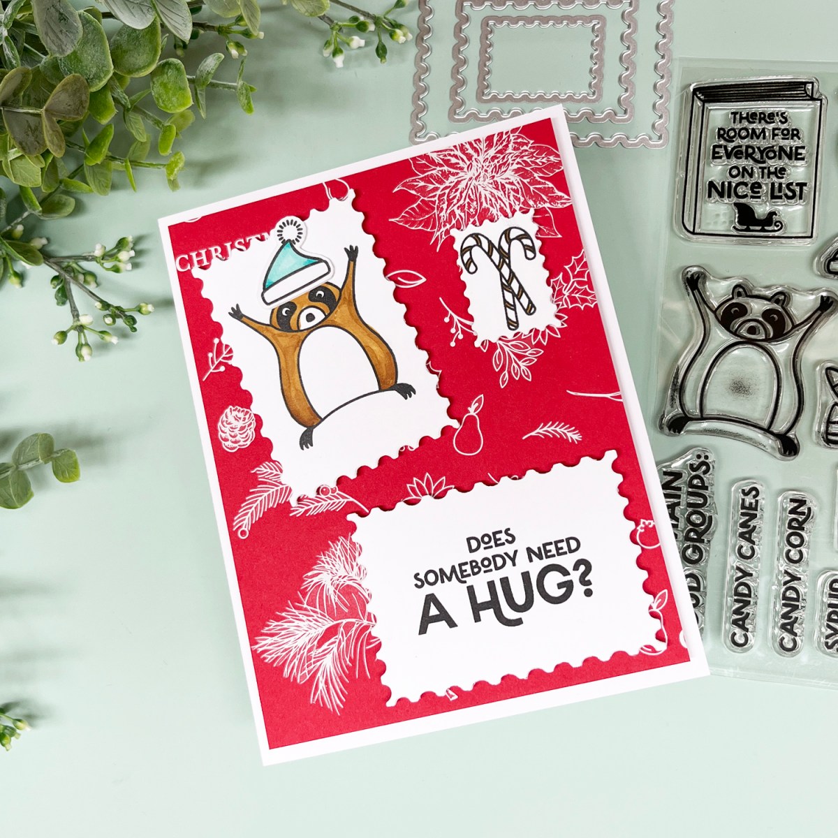 Adorable Christmas card with a raccoon reaching for a hug and the sentiment "Does Anybody Need a Hug?".  Bright red and white Hero Transfer rub-on background with three stamped and postage stamp die cut focal elements. 