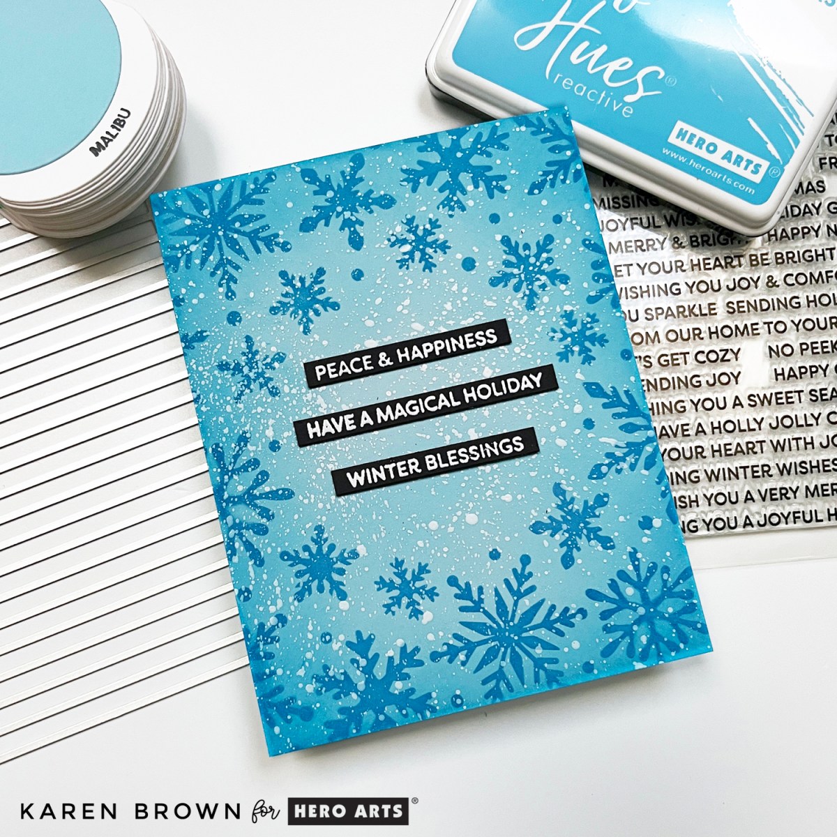 Blue snowflake stenciled handmade Christmas card with sentiments strips and white acrylic speckle.