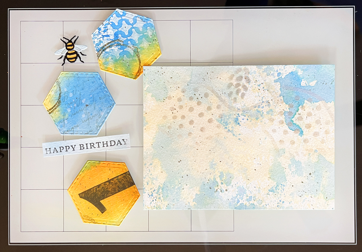 Process photo showing mixed media card components ready to assemble with a beautiful metallic heat embossing glow on the watercolor background panel.