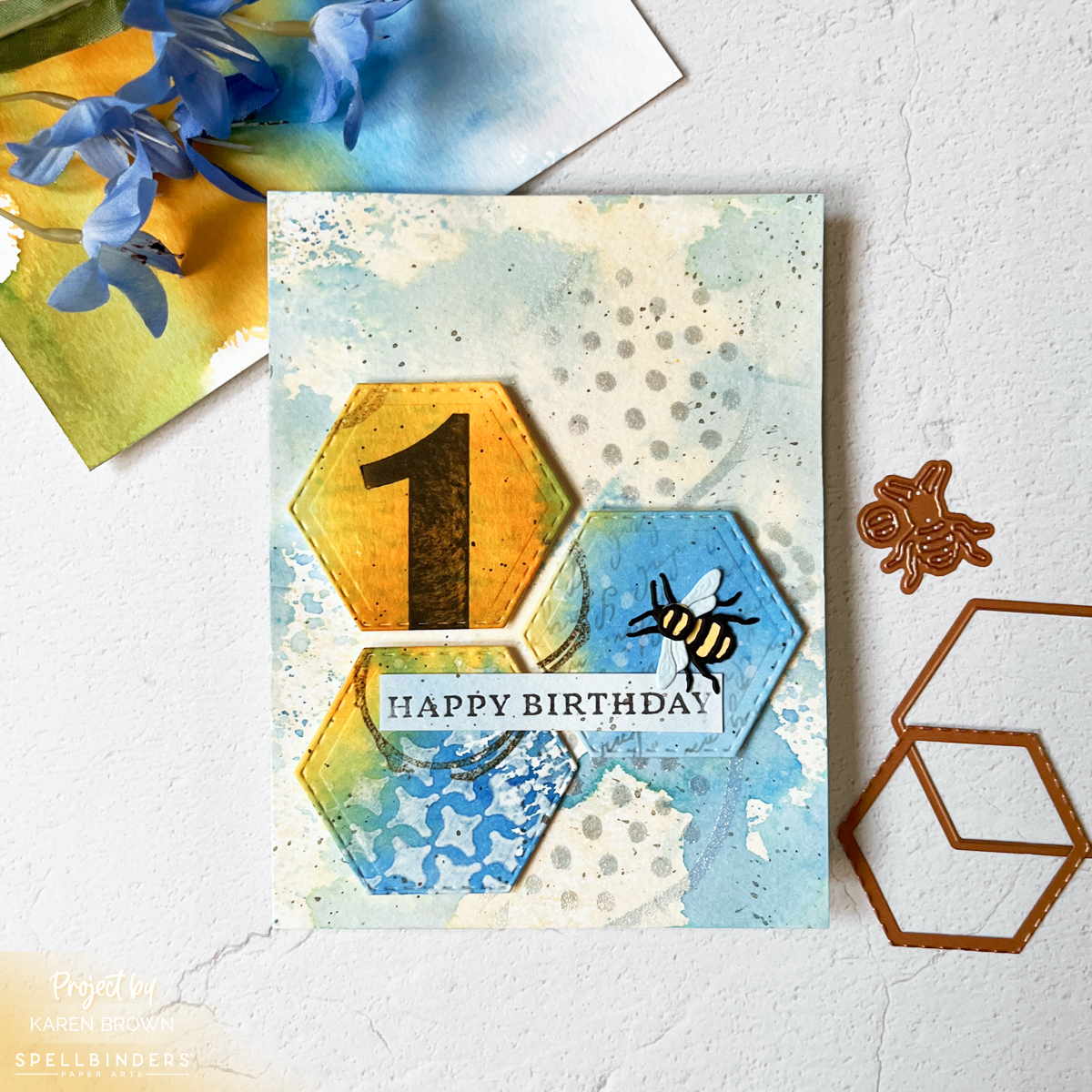 Mixed media birthday card featuring blue and honey gold ink smoosh backgrounds, layered stamping and stenciling, stitched hexagon die cuts, and a small bee embellishment.