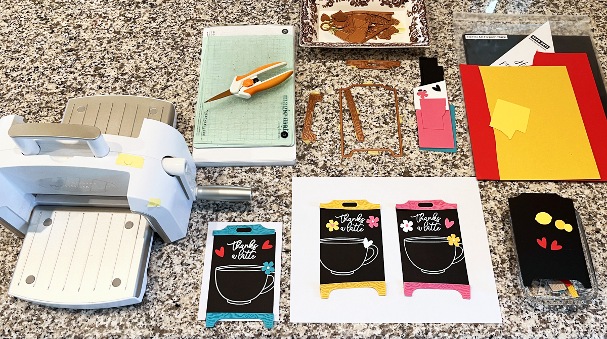 Process photo showing chalkboard card layouts, dies, cardstock, and die cutting machine