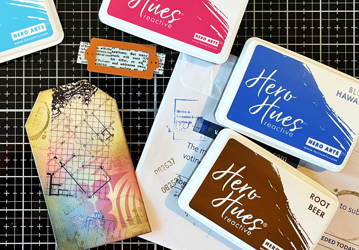 Process photo of ink blending on tan mixed media watercolor tag with detail of Hero Arts grid rub-on transfer and stamping.