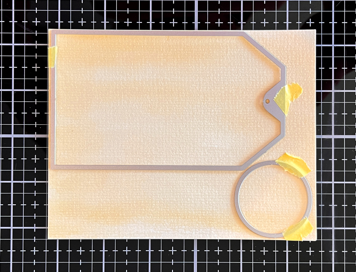 Process photo of mixed media tan watercolor wash tag background.