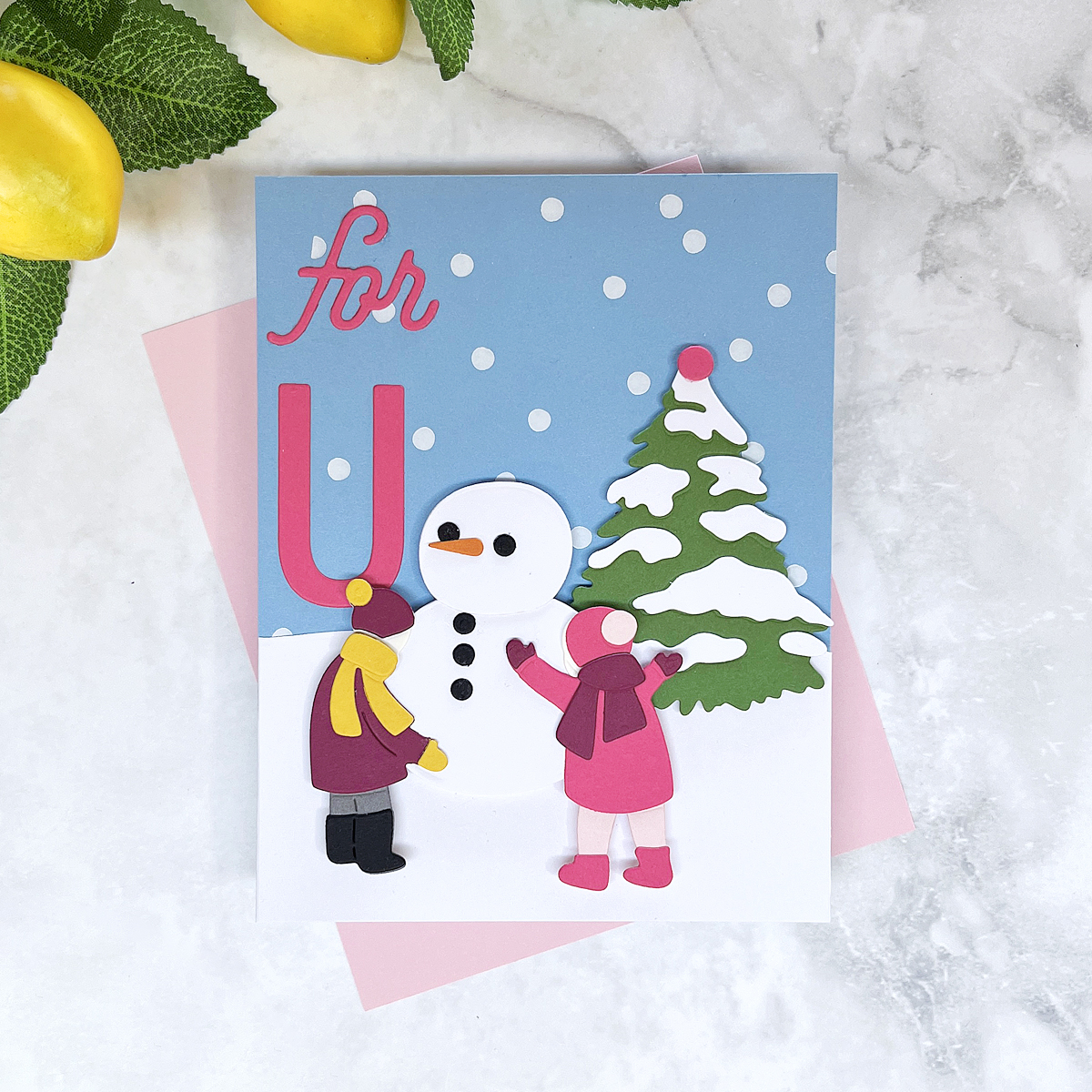 Die cut winter scene card of two children building a snowman.