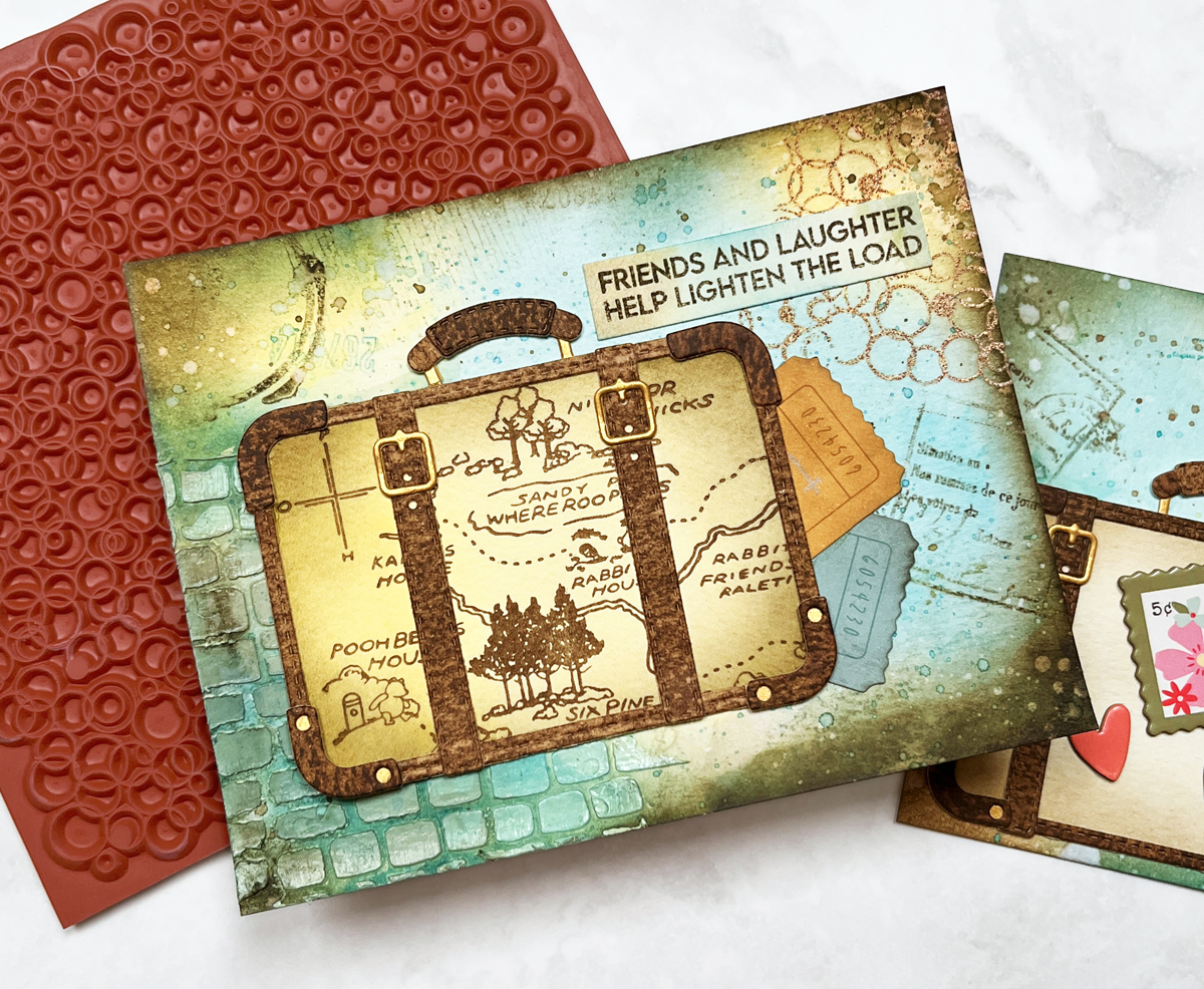 Mixed media card with layered watercolor background, texture paste, stamping, embossing and vintage suitcase focal point