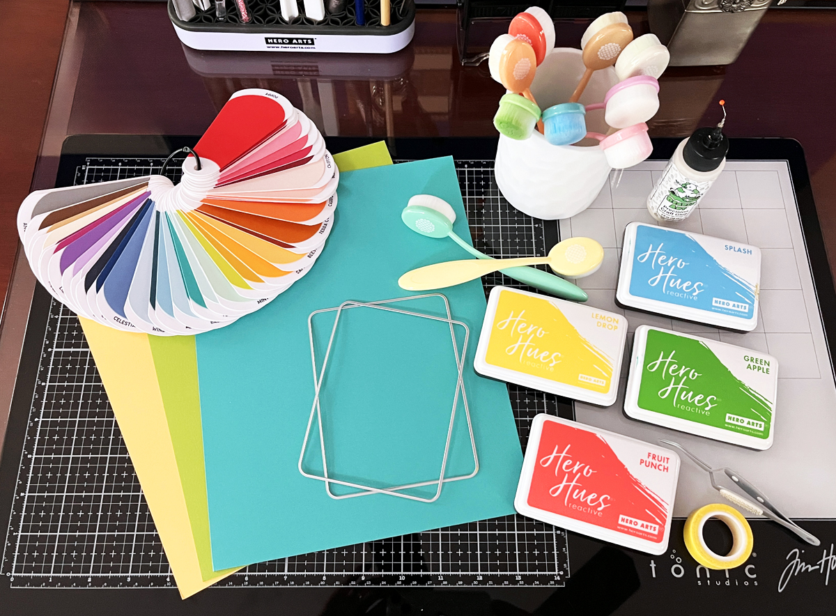 Craft desk with cardmaking supplies:  cardstock, ink, glue, blending brushes and color swatches.
