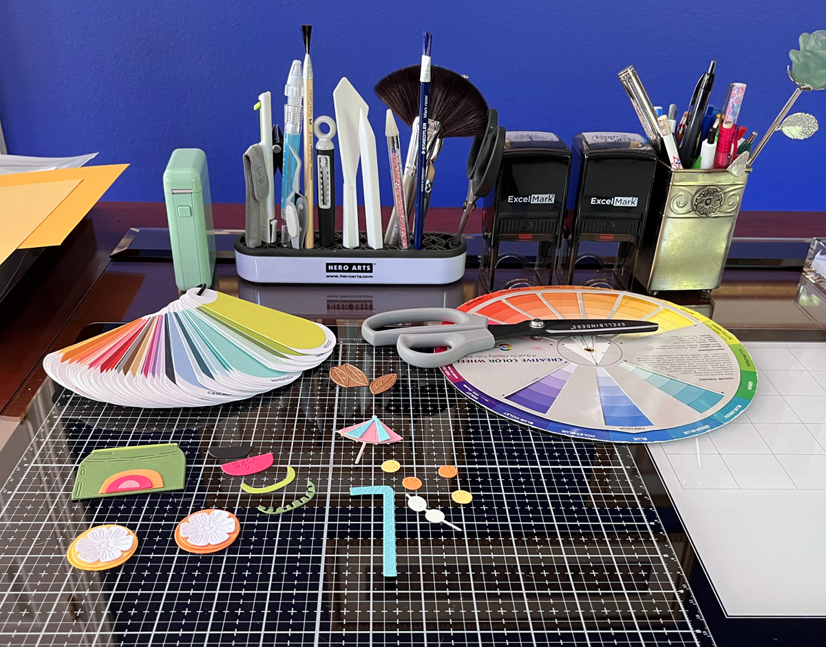Die cut card elements arranged on craft desk before assembly including citrus shapes and drink accents
