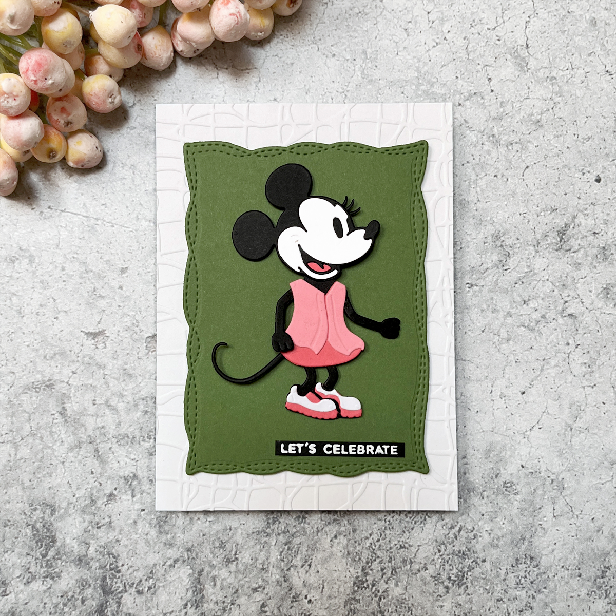 Minnie-inspired die cut with layered pink cardstock and black accents on green stitched mat and embossed white background