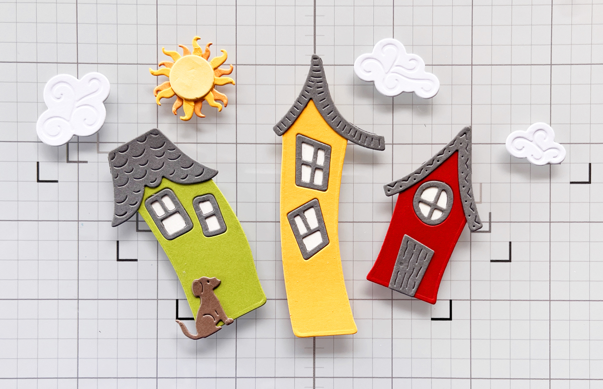 Die cut houses for handmade card with colorful fun elements layed out on a craft mat