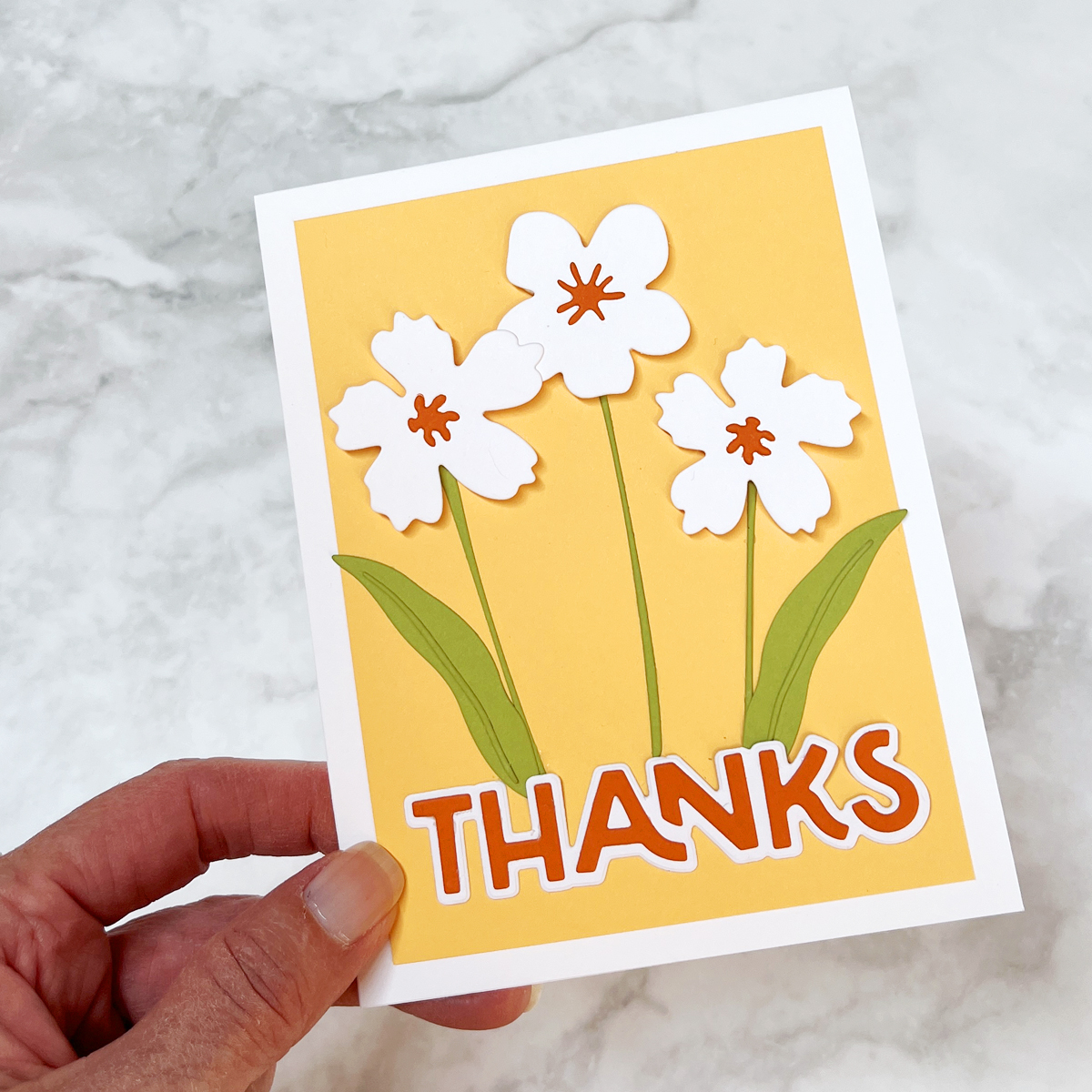 Clean and simple floral thank you card featuring white die cut blooms, orange thanks sentiment, and a cheerful yellow background.