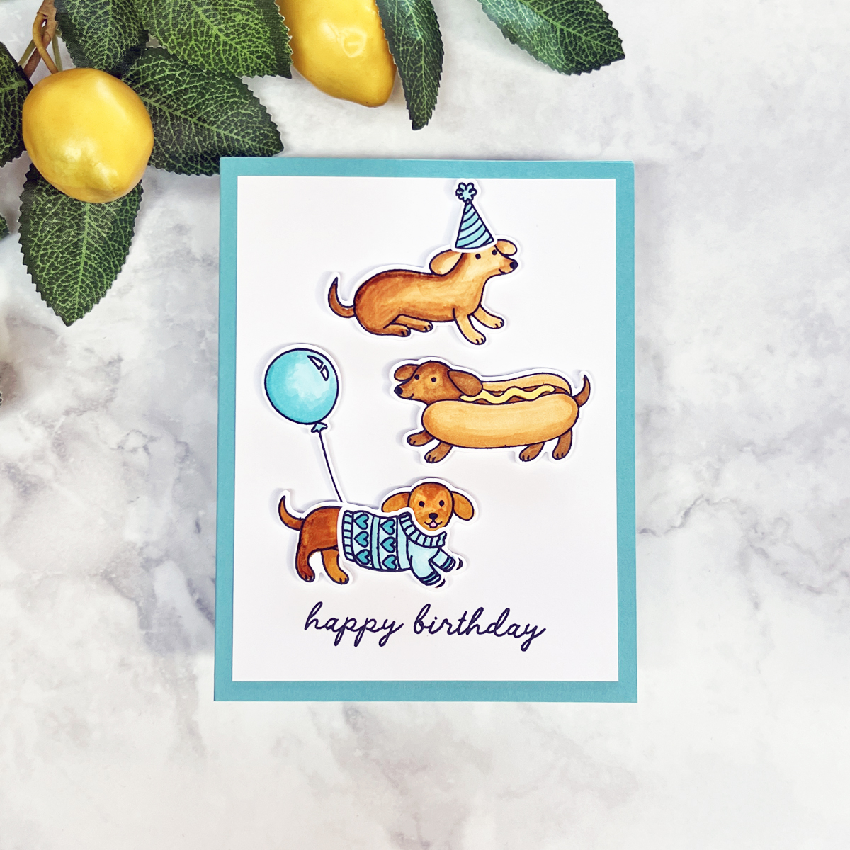 Playful handmade birthday card featuring three dachshund dog stamps with party accessories on an aqua card base.