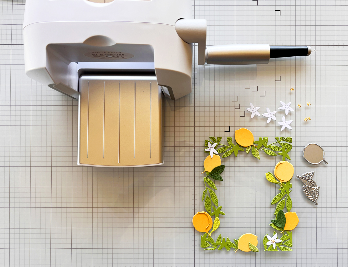 Die-cut citrus frame pieces, lemons, and leaves arranged on a craft mat next to a Scout desktop die-cutting machine.