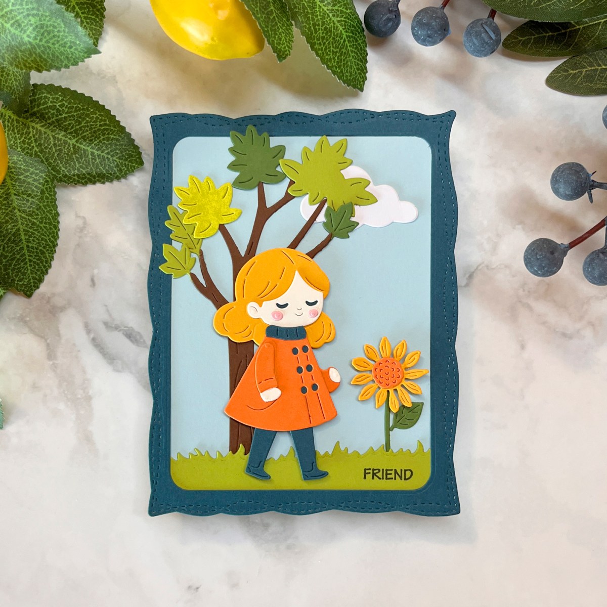 Die-cut outdoor scene card with atree, girl in a coat and sunflower.