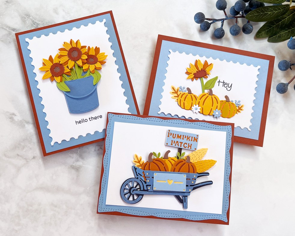 3 seasonal Fall handmade cards featuring a wheelbarrow full of pumpins, a blue bucket with 3 sunflowers and mini pumpkin patch with a cheerful sunflower. The color palette is slate blue, rusty orange and yellow.
