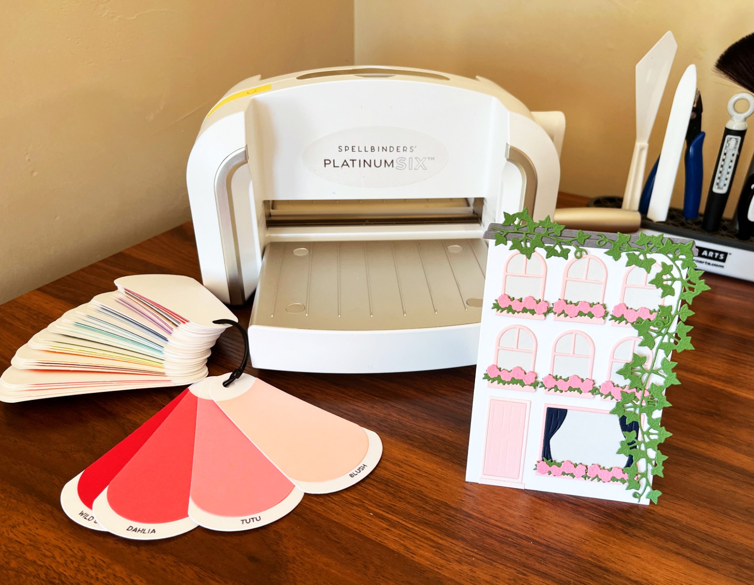 Die cut card sitting in front of a Platinum 6 die-cutting machine and cardstock swatches.