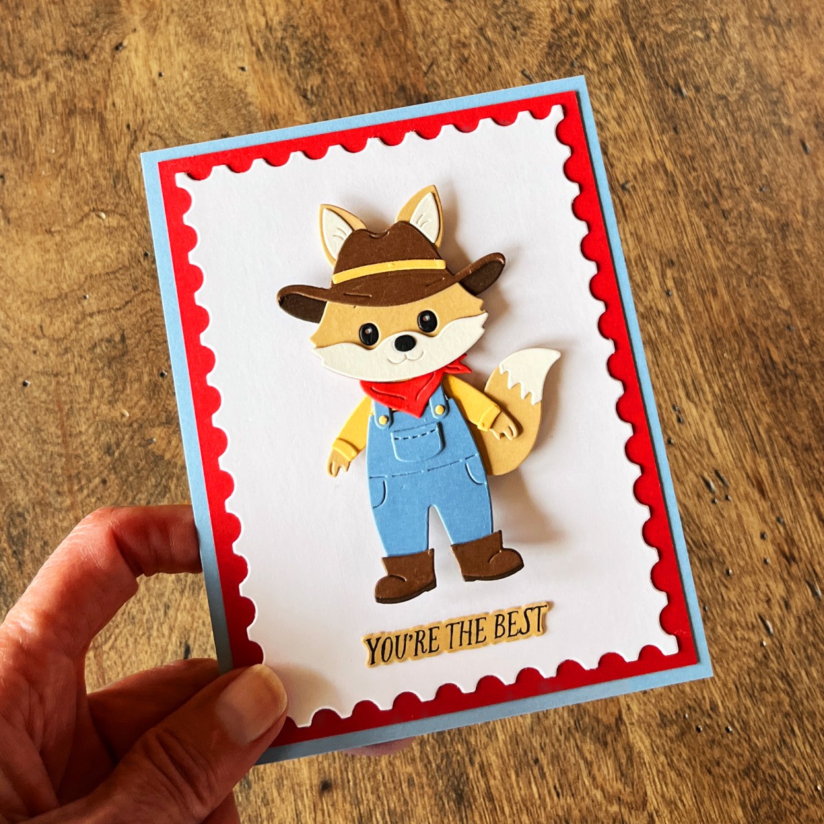 Die cut animal card featuring a cute fox in denim overalls and a red kerchief with a red and blue layered background.