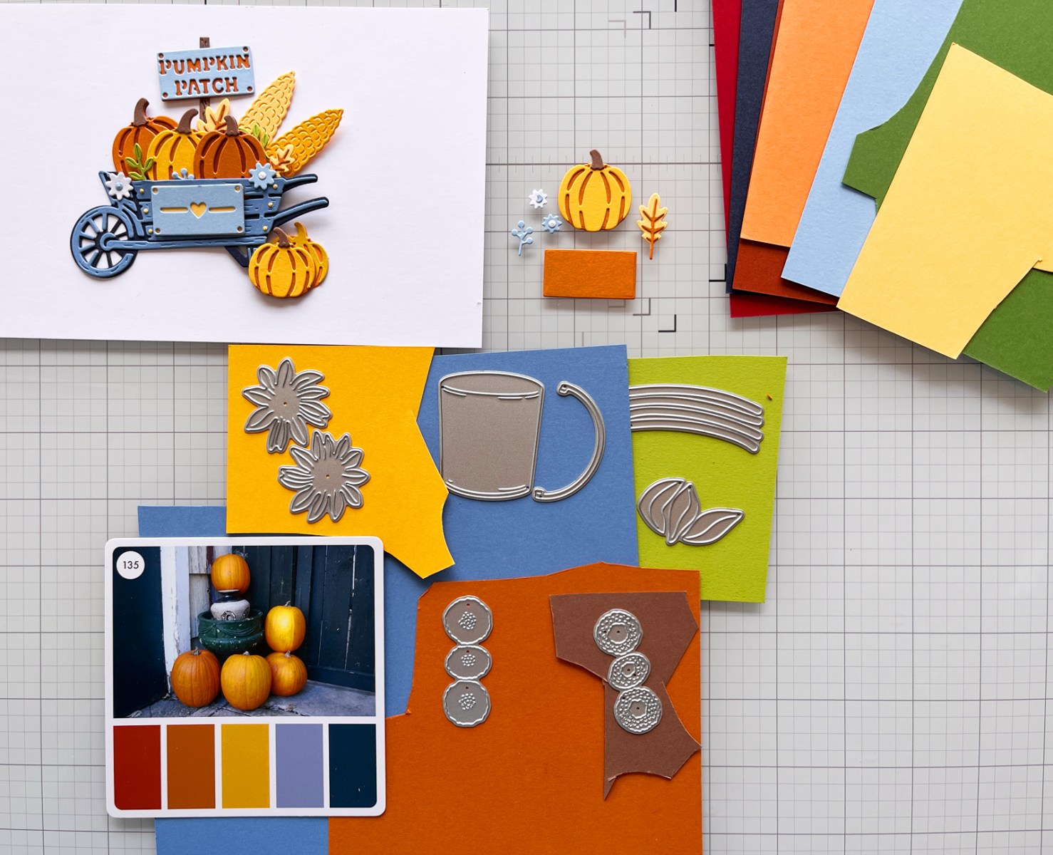 Two handmade cards being planned on a craft mat with die-cut pieces, cardstock and a Color Cube inspiration card in view.